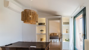 Een eetruimte met een houten tafel en transparante stoelen, een hanglamp en een boekenplank op de achtergrond.