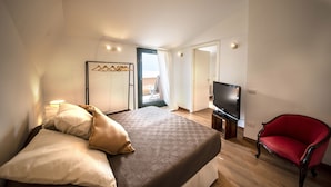 Een hotelkamer met een bed, een televisie, een rode stoel en uitzicht op een balkon.