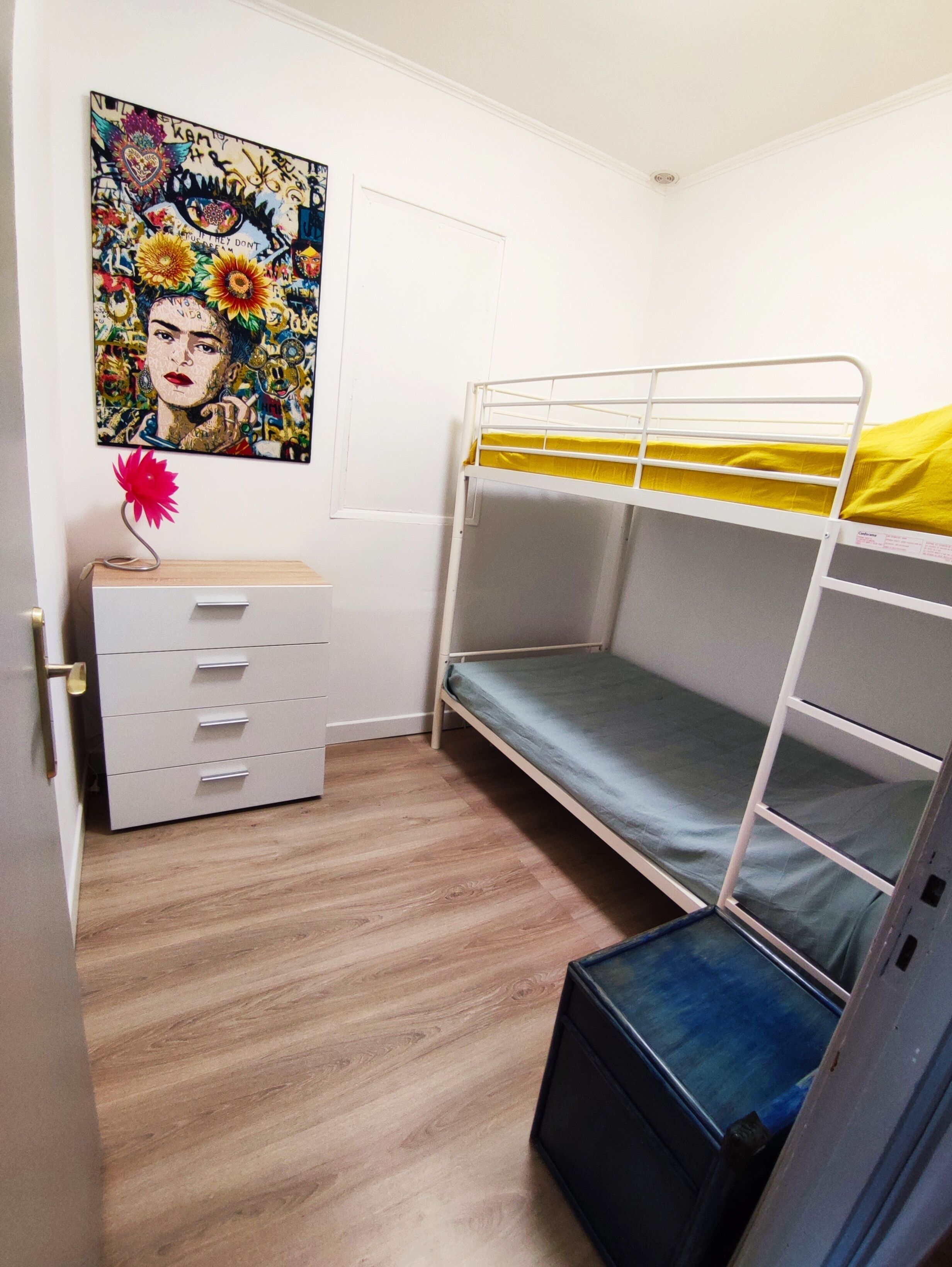 A bunk bed room with a white dresser, a colorful painting, and a small red flower vase.