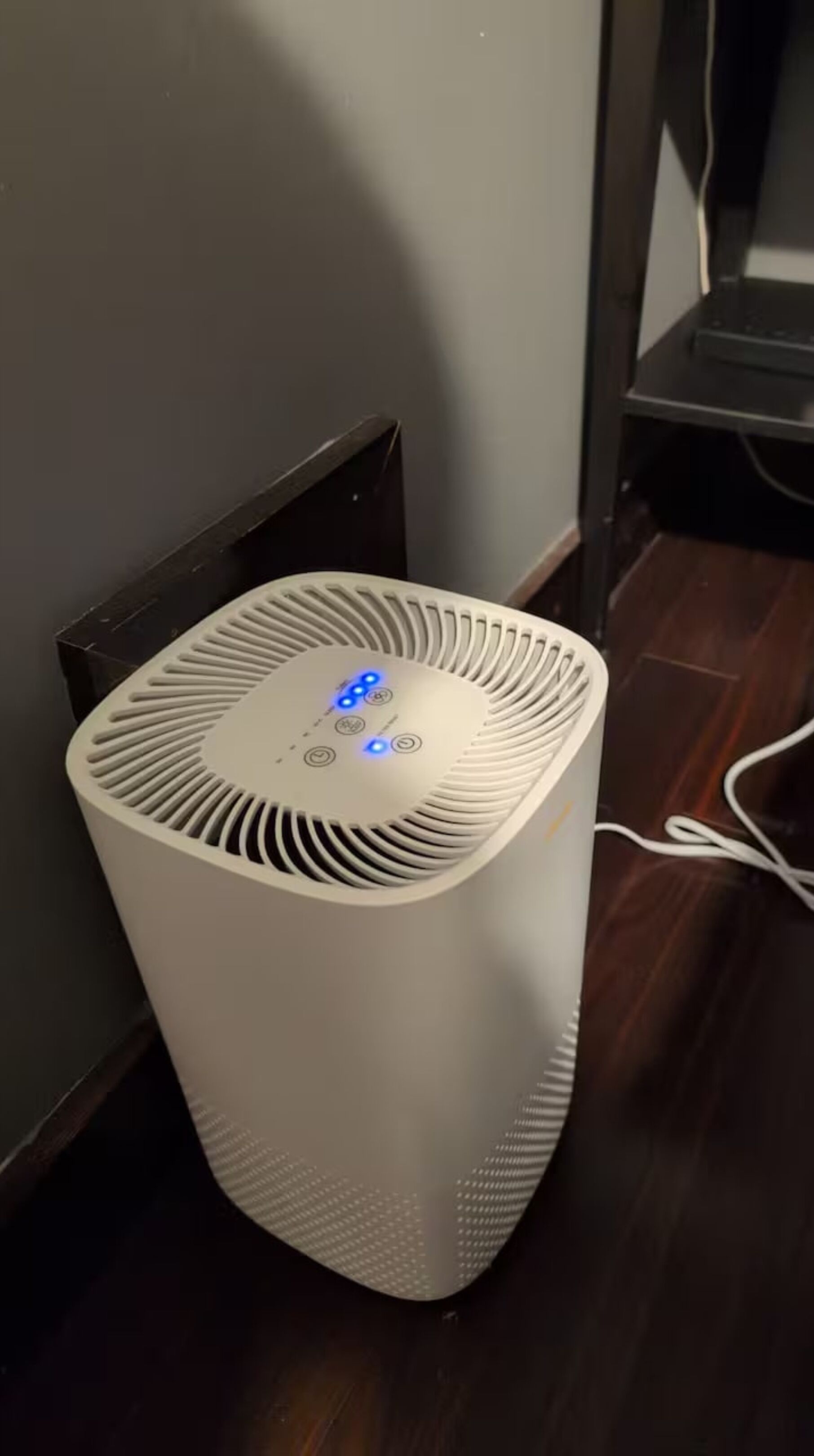 Un radiateur vertical blanc, doté d’un panneau de commande et de lumières bleues, est placé contre un mur dans une pièce dont le sol est recouvert de parquet.