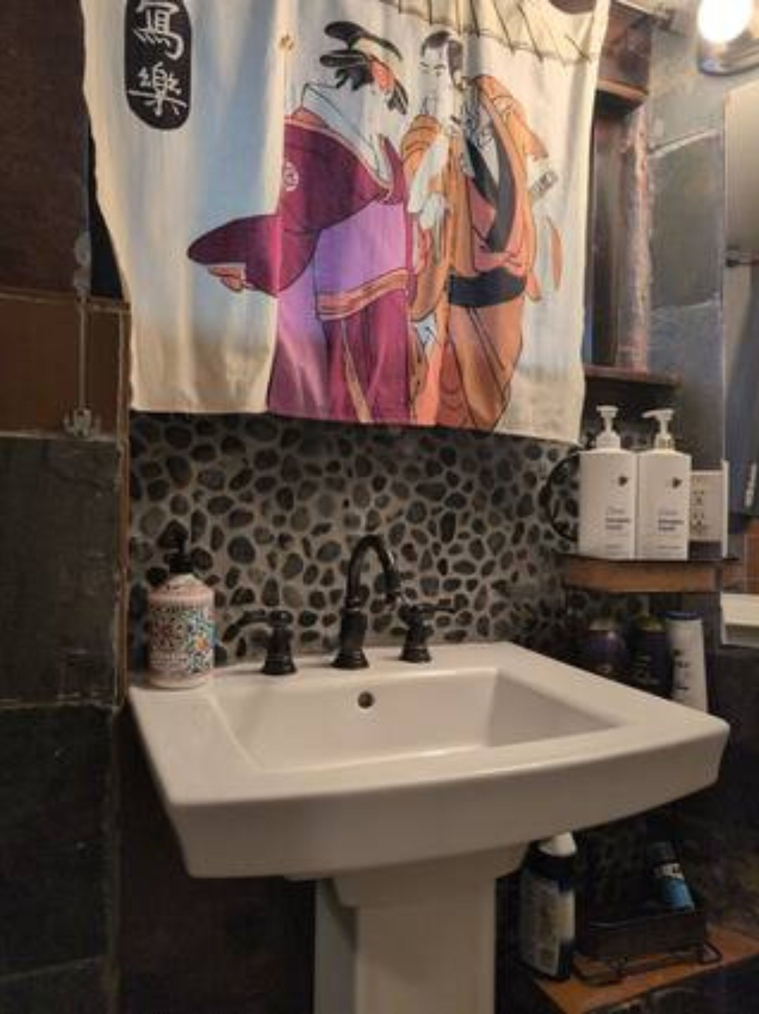 Ein Badezimmer mit Waschbecken, einem Deko-Handtuch mit traditionellem Muster und Pflegeprodukten auf einem Regal.