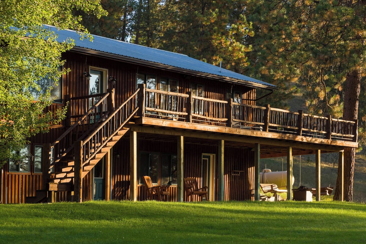 A two-story wooden cabin with a balcony, outdoor seating, and a covered porch.