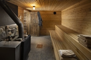 A sauna room with wooden walls, a bench, a towel rack, and a stone wall.
