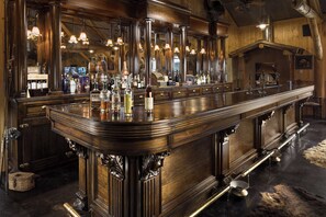 A bar with a polished wooden counter, bottles, and a large mirror.