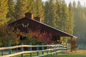 A rustic barn with a wooden exterior and a large eagle emblem, surrounded by a wooden fence and trees.