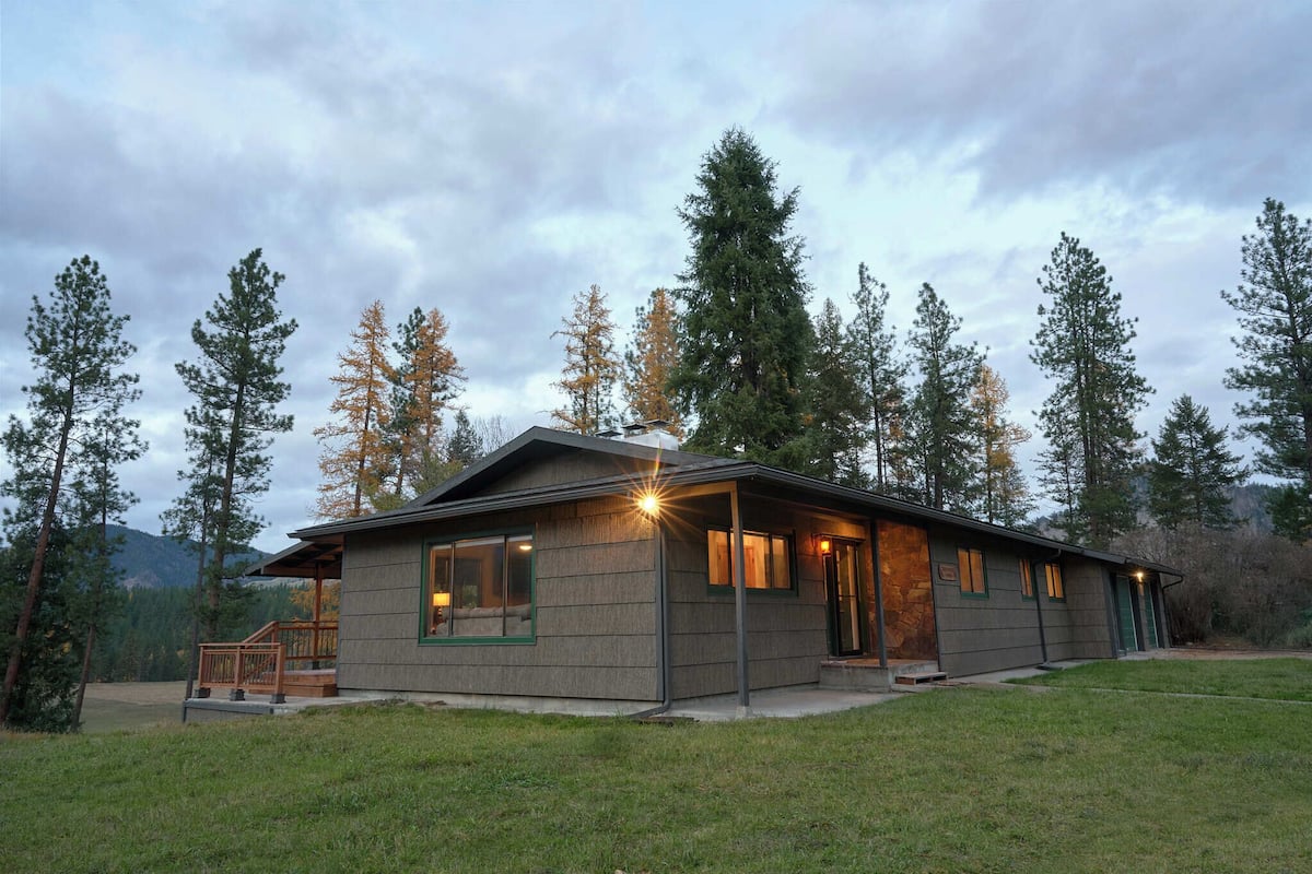 A two-story lodge with a porch, large windows, and a stone fireplace.
