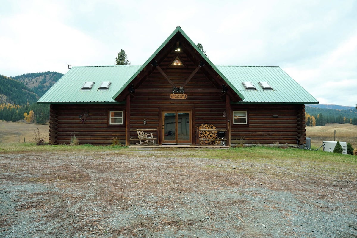 A rustic log cabin with a green metal roof, a front porch with a bench, and a sign that reads "Peace Bear Gulch."