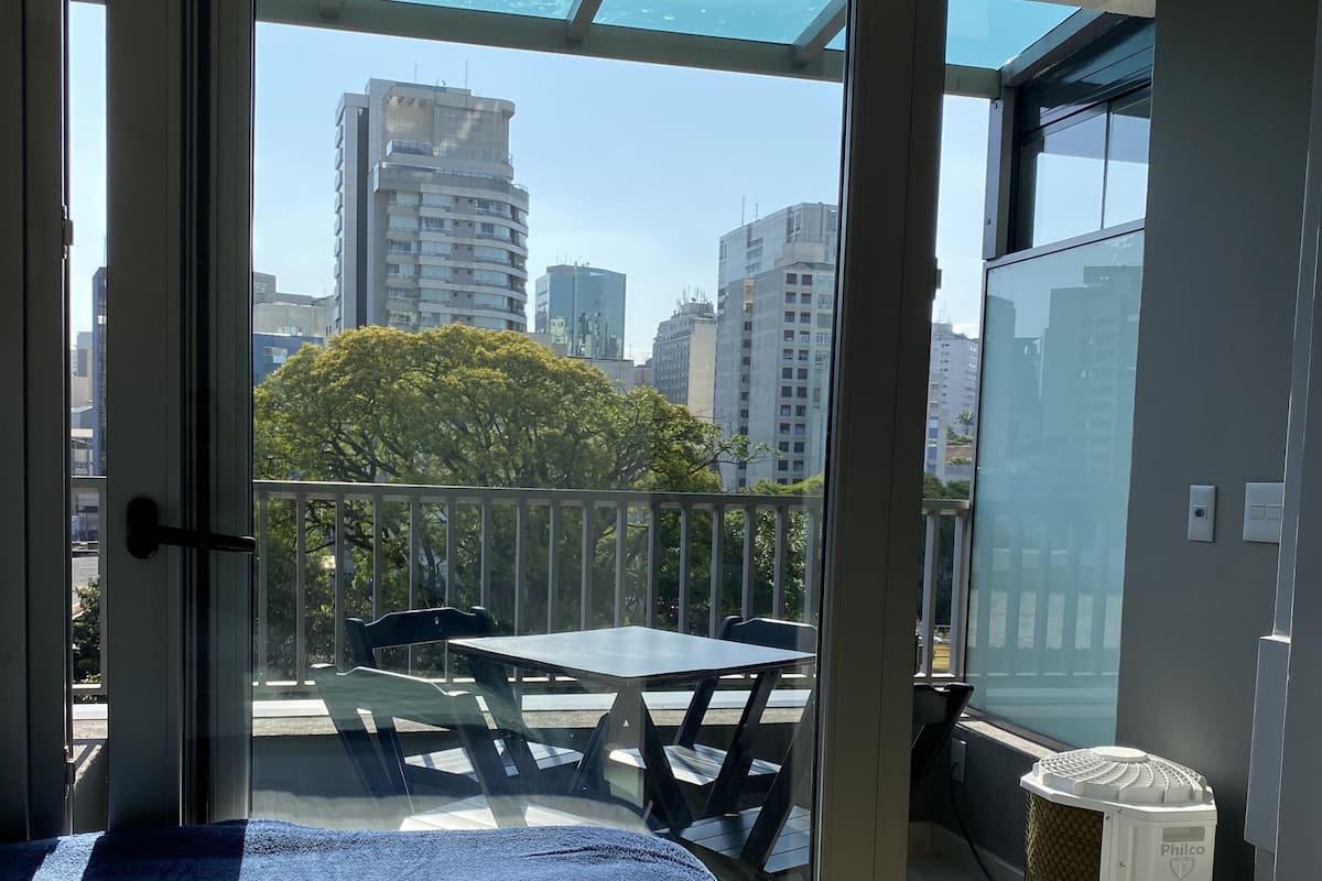 Une chambre avec un lit, un balcon avec une table et des chaises, et une vue sur le paysage urbain.