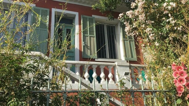 Een rood gebouw met groene luiken, een wit balkon en roze bloemen.