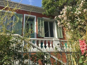 Un bâtiment rouge avec des volets verts, un balcon blanc et des fleurs roses.
