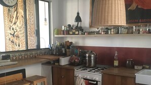 Een keuken met houten kastjes, een gasfornuis, een hangende lamp en een klok aan de muur.