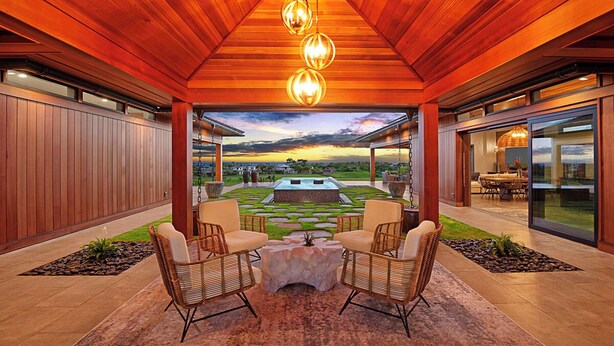A covered outdoor seating area with wicker chairs and a central table, overlooking a pool and garden. - Hale Kupanaha: Opulent New Villa + Pool/Spa/Views (Koloa)