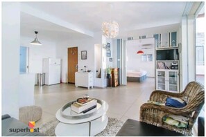 A modern living room with a round coffee table, a wicker sofa, and a bookshelf. - Stunning Rooftop apartment on Hayarkon St (Tel Aviv-Yafo)