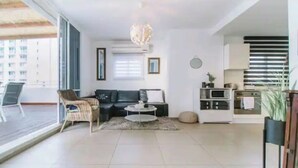 A modern living room with a sofa, coffee table, and a dining area with a microwave. - Stunning Rooftop apartment on Hayarkon St (Tel Aviv-Yafo)