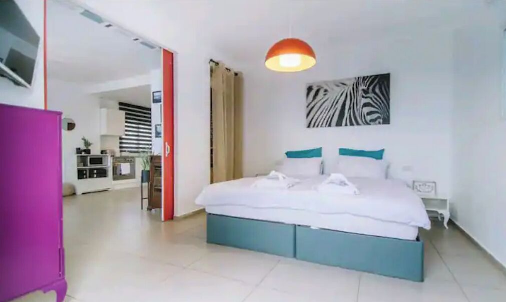 Une chambre d’hôtel comprenant un lit, un bureau, une chaise, une fenêtre avec des rideaux et une œuvre d’art accrochée au mur.