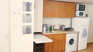 Une cuisine compacte dotée de meubles en bois, d’un four à micro-ondes, d’un lave-linge et d’un petit plan de travail sur lequel sont disposés divers objets.