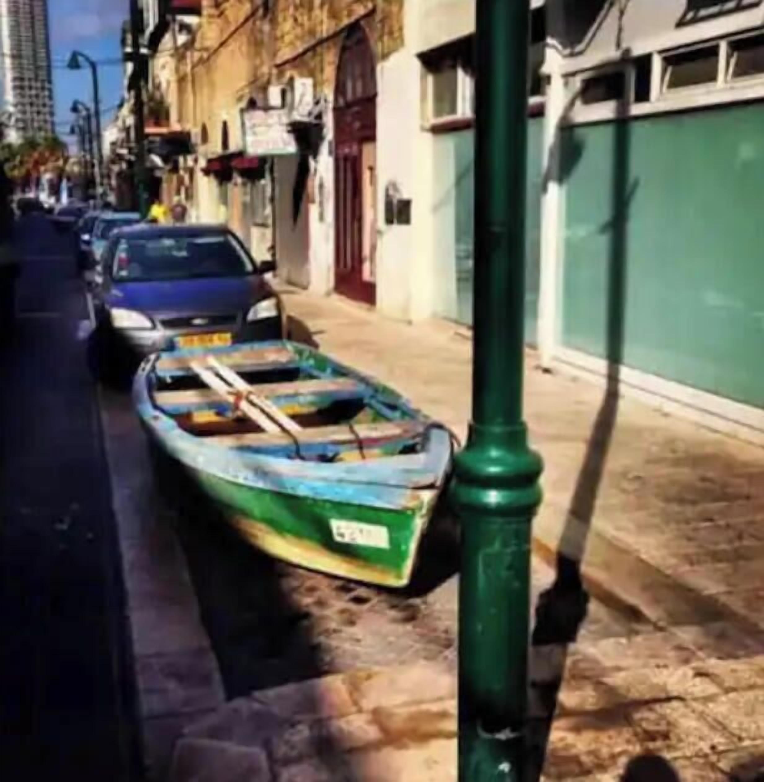 Une rue étroite, bordée de voitures garées, et un petit bateau amarré à un poteau vert.