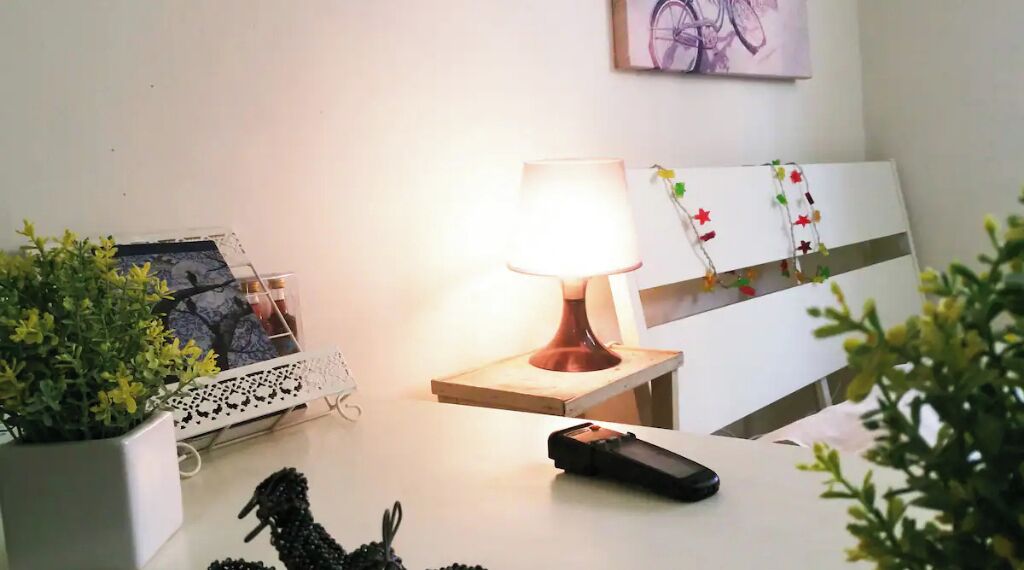 Ein gut beleuchteter Raum mit einer Lampe auf einem Holztisch, einem gerahmten Foto an der Wand und einer Topfpflanze.