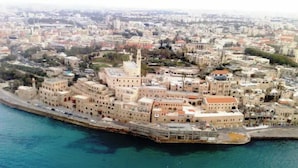Une vue aérienne d’une ville côtière, avec une zone riveraine bien visible, où se côtoient une architecture traditionnelle et moderne, une église imposante et une vue dégagée sur la mer.