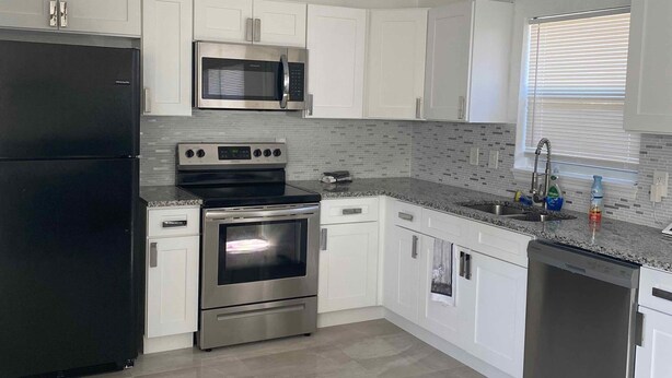 A modern kitchen with white cabinets, stainless steel appliances, and a tiled backsplash. - Clearwater Home Away from Home (Clearwater)