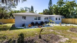 A single-story house with a grey exterior, a front yard with various plants, and a wooden fence. - Clearwater Home Away from Home (Clearwater)