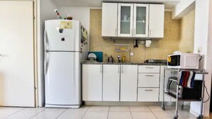 Cozinha com armários brancos, geladeira branca, micro-ondas e forno portátil sobre um carrinho.