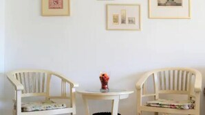 Um quarto com duas cadeiras de madeira e uma pequena mesa redonda, com quadros nas paredes.