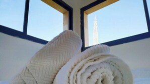 Cama com toalhas brancas dobradas e janela com vista para uma construção alta.