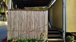 Un'area esterna coperta con recinzione in legno, scalini che portano a una porta e piante in vaso.