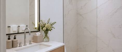 Un baño moderno con ducha de mármol, lavabo con artículos de aseo y retrete.