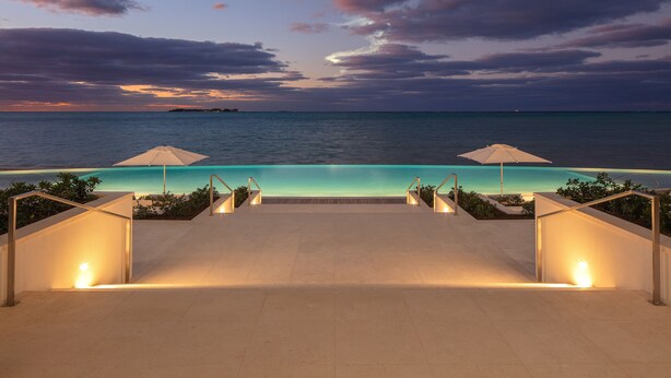 An infinity pool with two umbrellas, a clear view of the ocean, and a sunset sky. - Goldwynn Resort & Residences (Nassau)