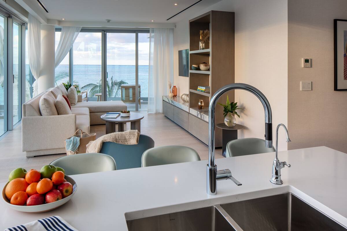 A modern living room with a large window, a sofa, a dining area, and a kitchen with a sink.