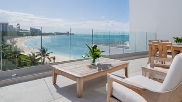 Un balcón con vista a la playa, una mesa de madera y dos sillas.