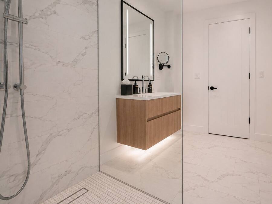 Ein modernes Badezimmer mit Duschkabine aus Glas, einem Holzwaschtisch, einem großen Spiegel und einer weißen Tür.