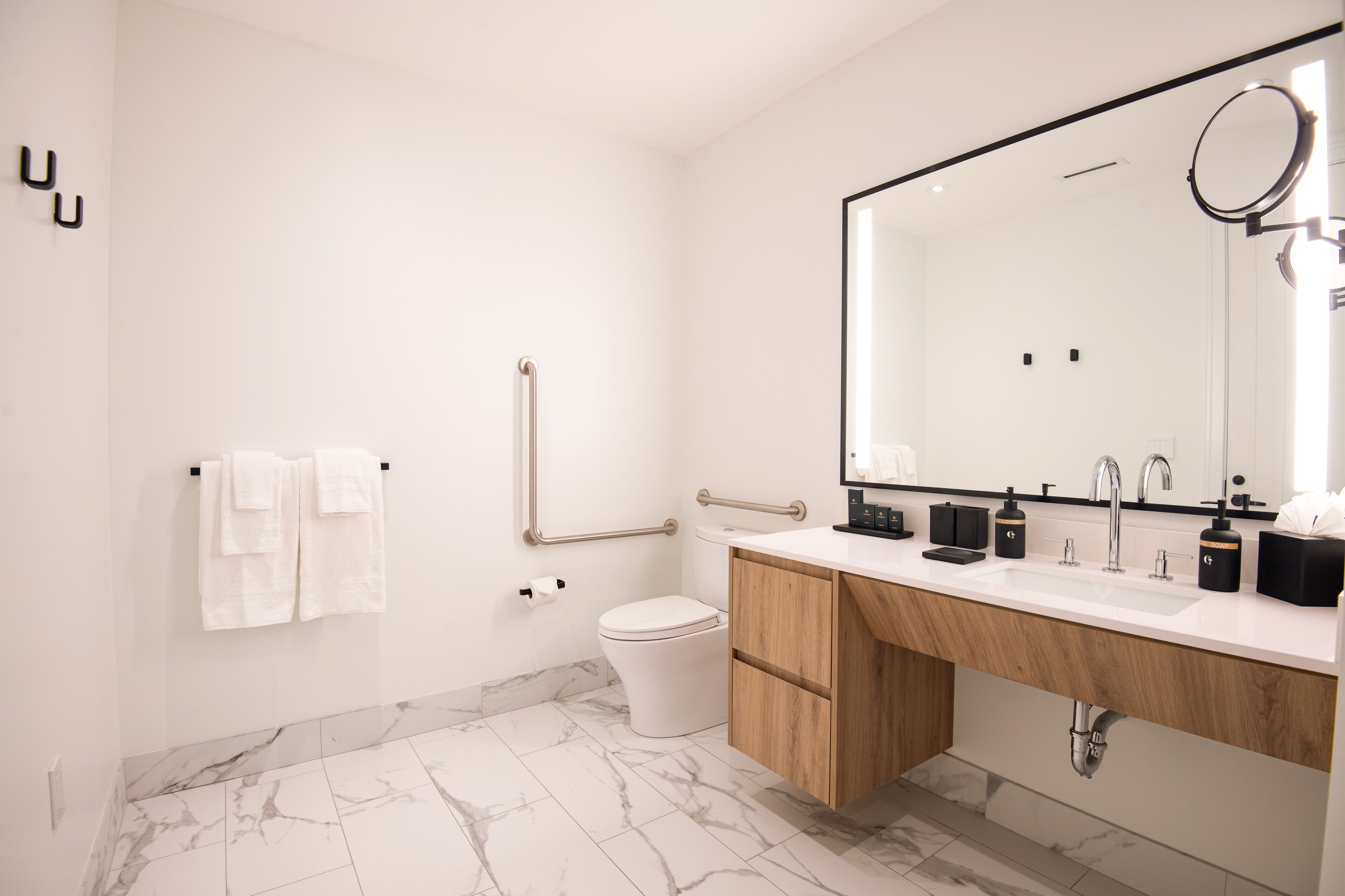 A modern bathroom with a marble floor, a white toilet, a wooden vanity, and a large mirror.