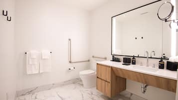 A modern bathroom with a marble floor, a white toilet, a wooden vanity, and a large mirror.