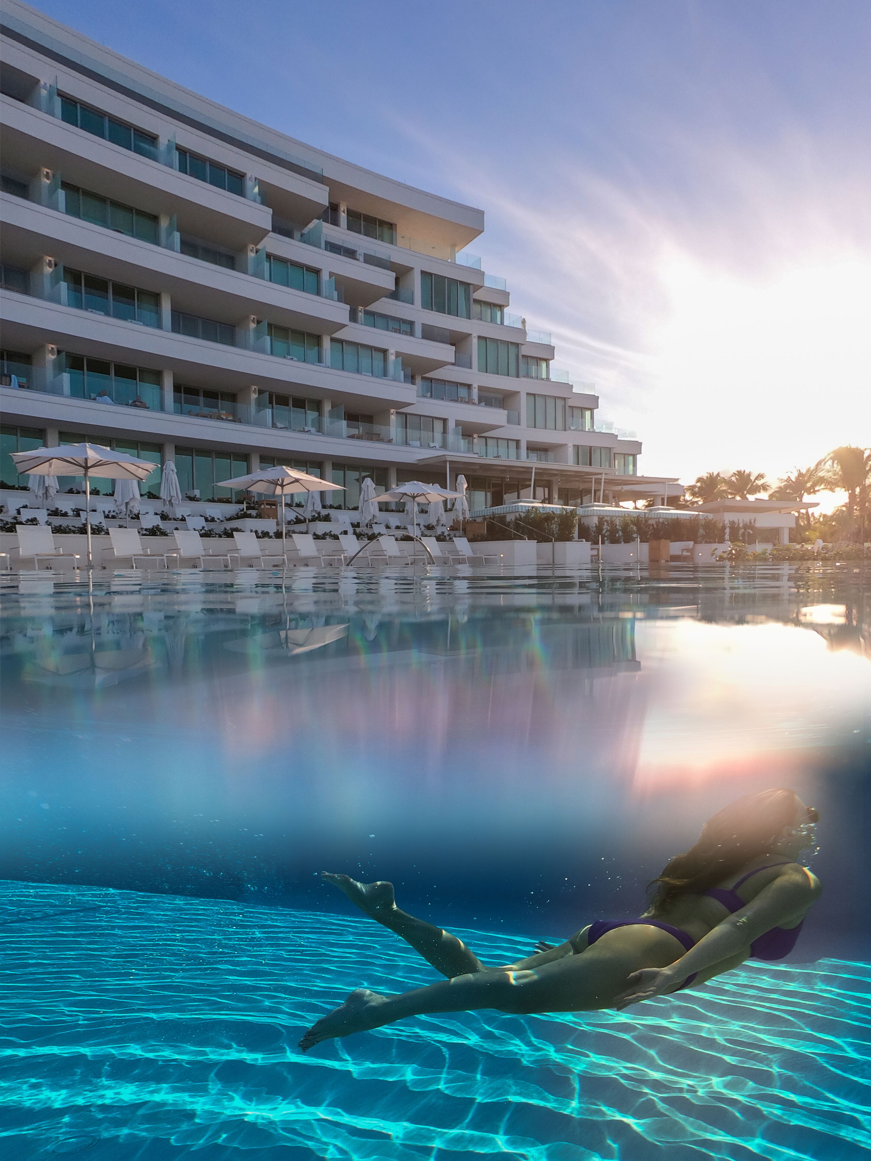 Un hotel moderno con piscina, tumbonas y sombrillas.