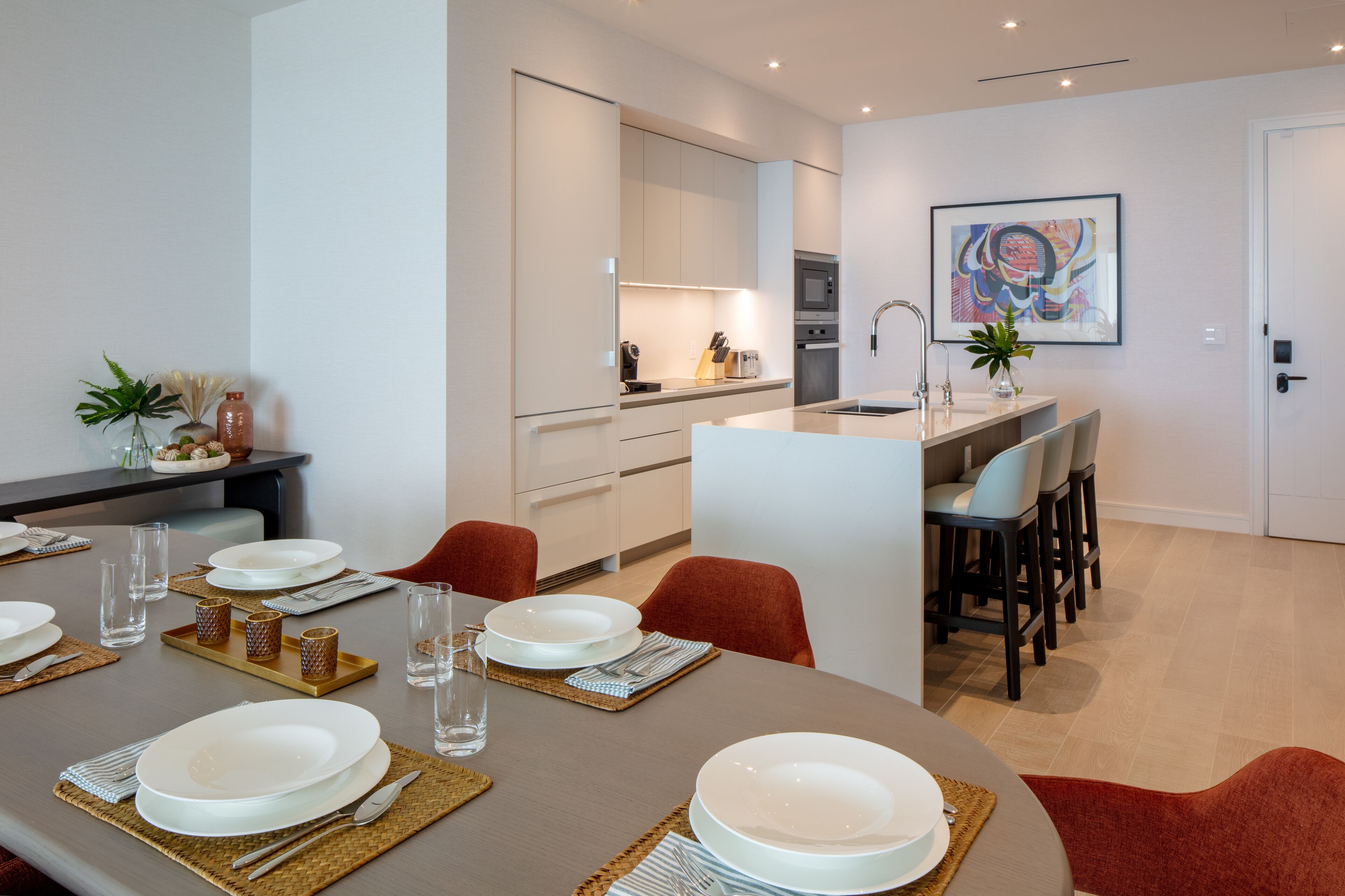 A modern dining area with a round table set for four, a kitchen adjacent to the dining area, and a small island with seating.