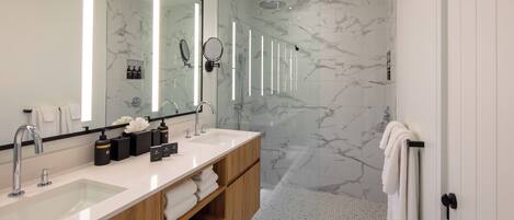 A modern bathroom with a large mirror, two sinks, a shower, and marble flooring.