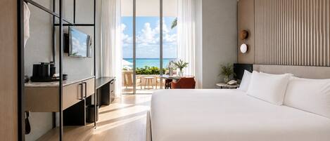 Habitación de hotel moderna con una cama grande, un escritorio con una silla, un televisor y vistas al océano.