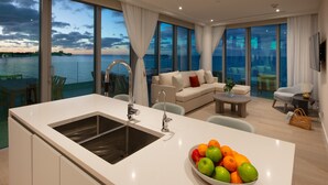 A modern kitchen with a large island, a dining area with a table and chairs, a sofa, and a view of the sea. - Goldwynn Resort & Residences (Nassau)