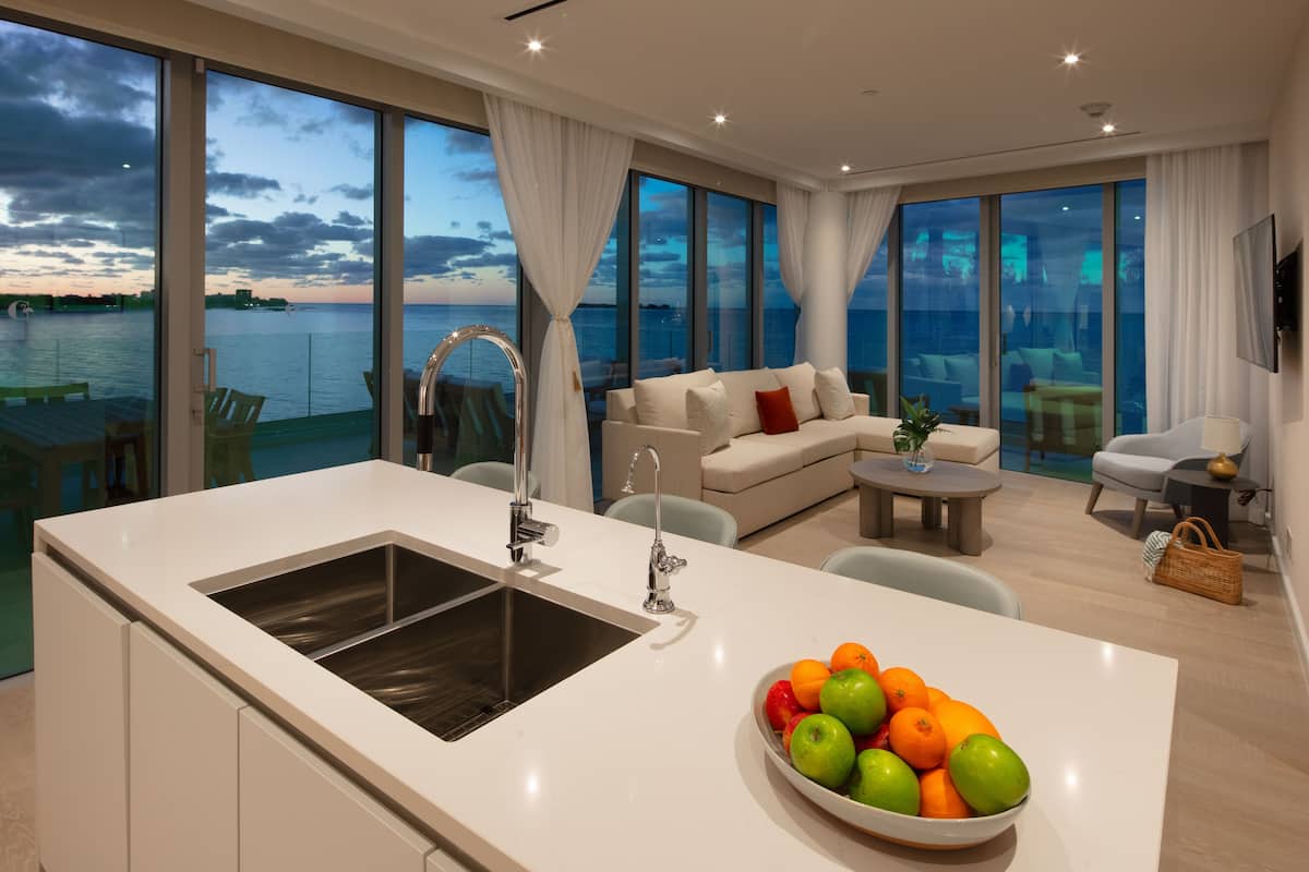 A modern kitchen with a large island, a dining area with a table and chairs, a sofa, and a view of the sea.