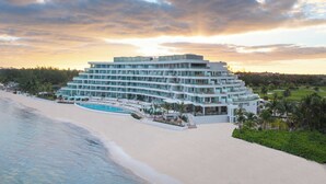 A multi-story hotel with a pool, located on a beach with a view of the ocean and a golf course in the background. - Goldwynn Resort & Residences (Nassau)