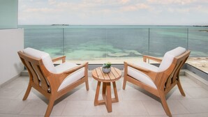A balcony with two wooden chairs and a small table, overlooking a clear blue sea and a distant island. - Goldwynn Resort & Residences (Nassau)