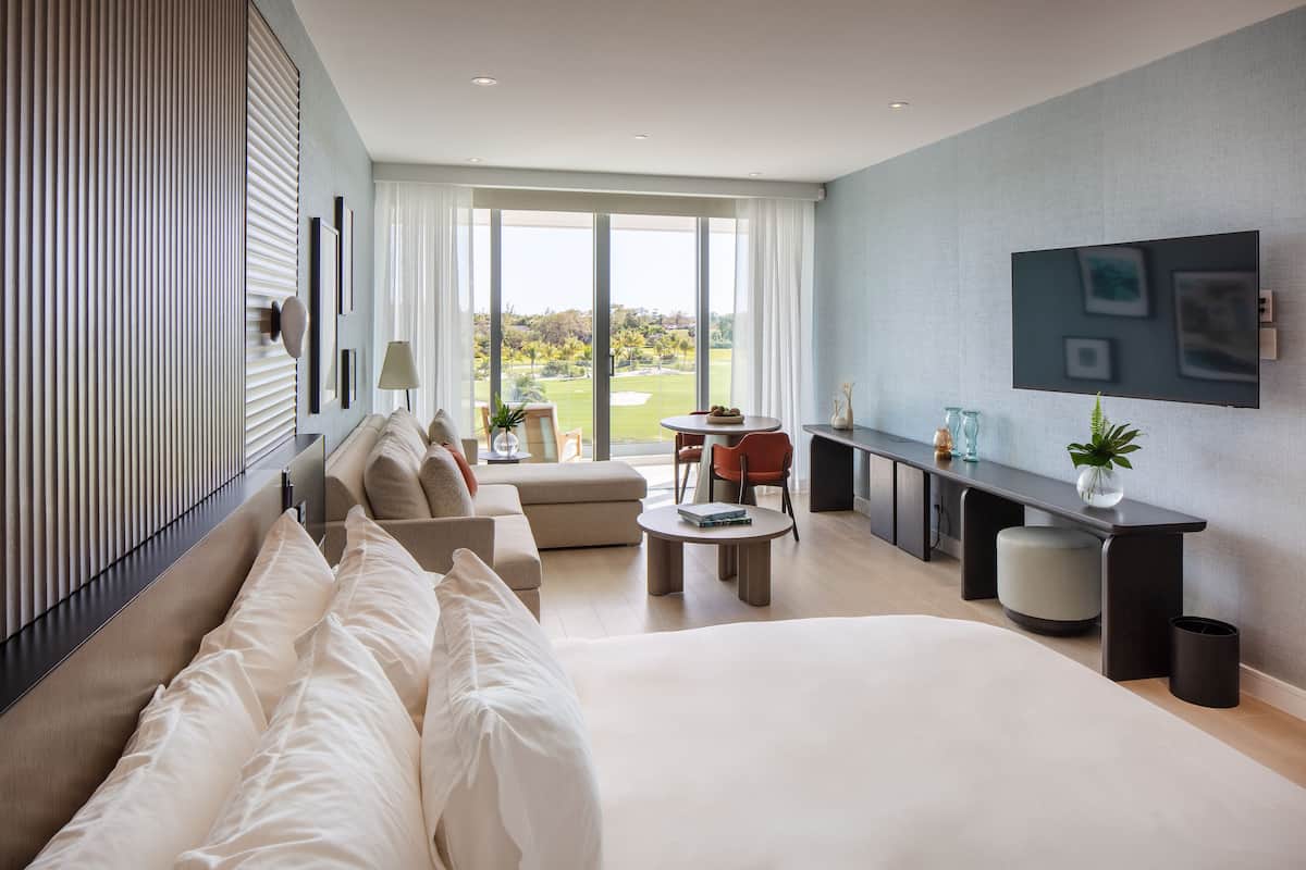 A modern hotel room with a large bed, a seating area with a table, and a TV on the wall.