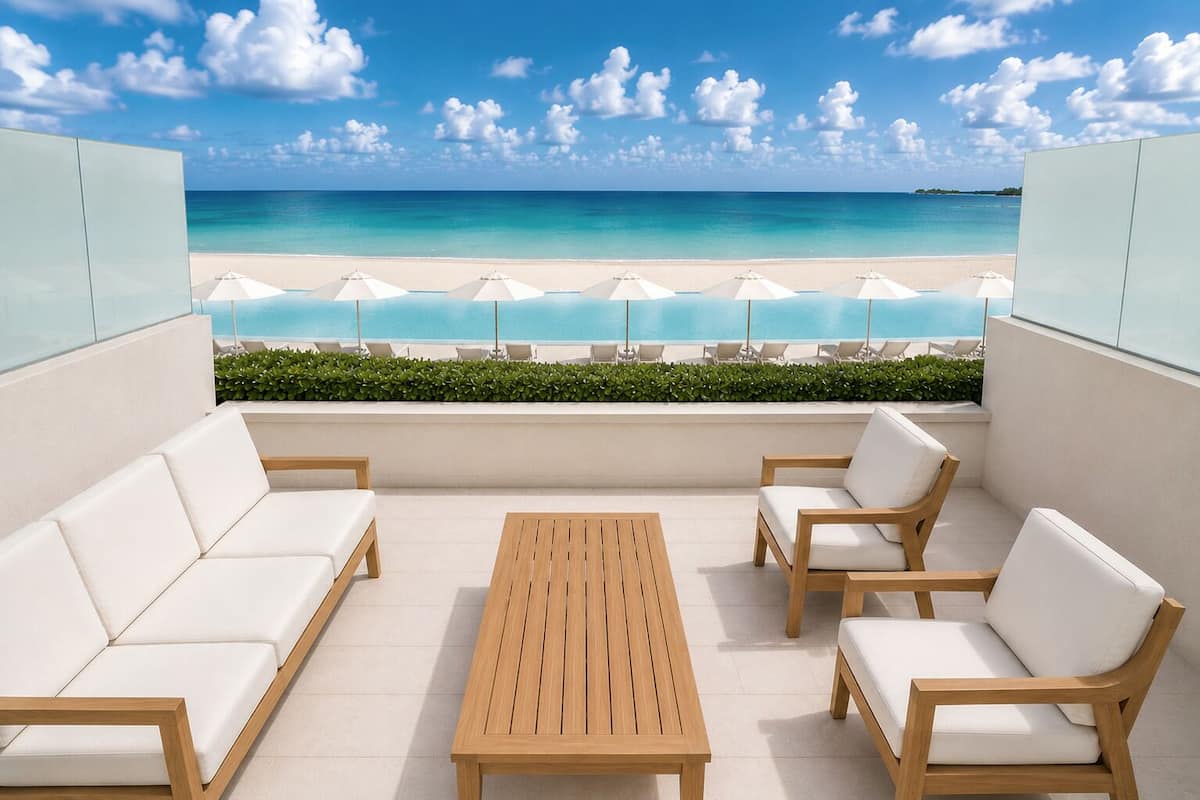 A balcony with a view of a beach, white outdoor furniture, and a wooden table.