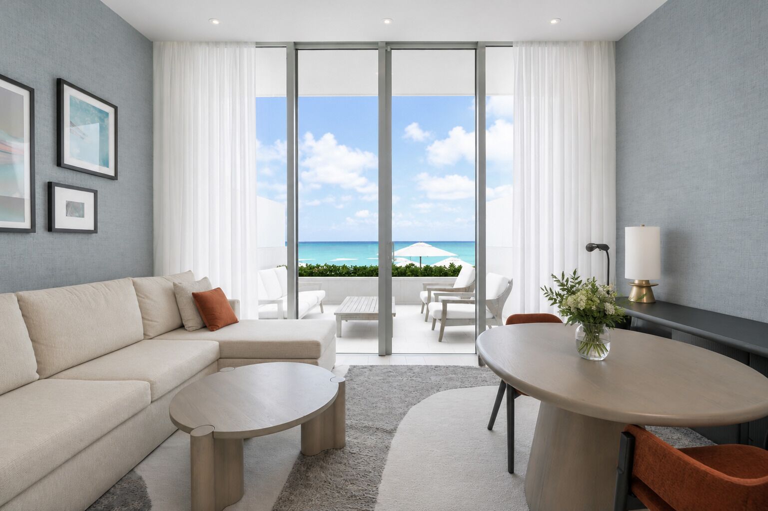 Quarto de hotel moderno com varanda, sofá, mesa de centro, mesa de jantar e vista para o mar.