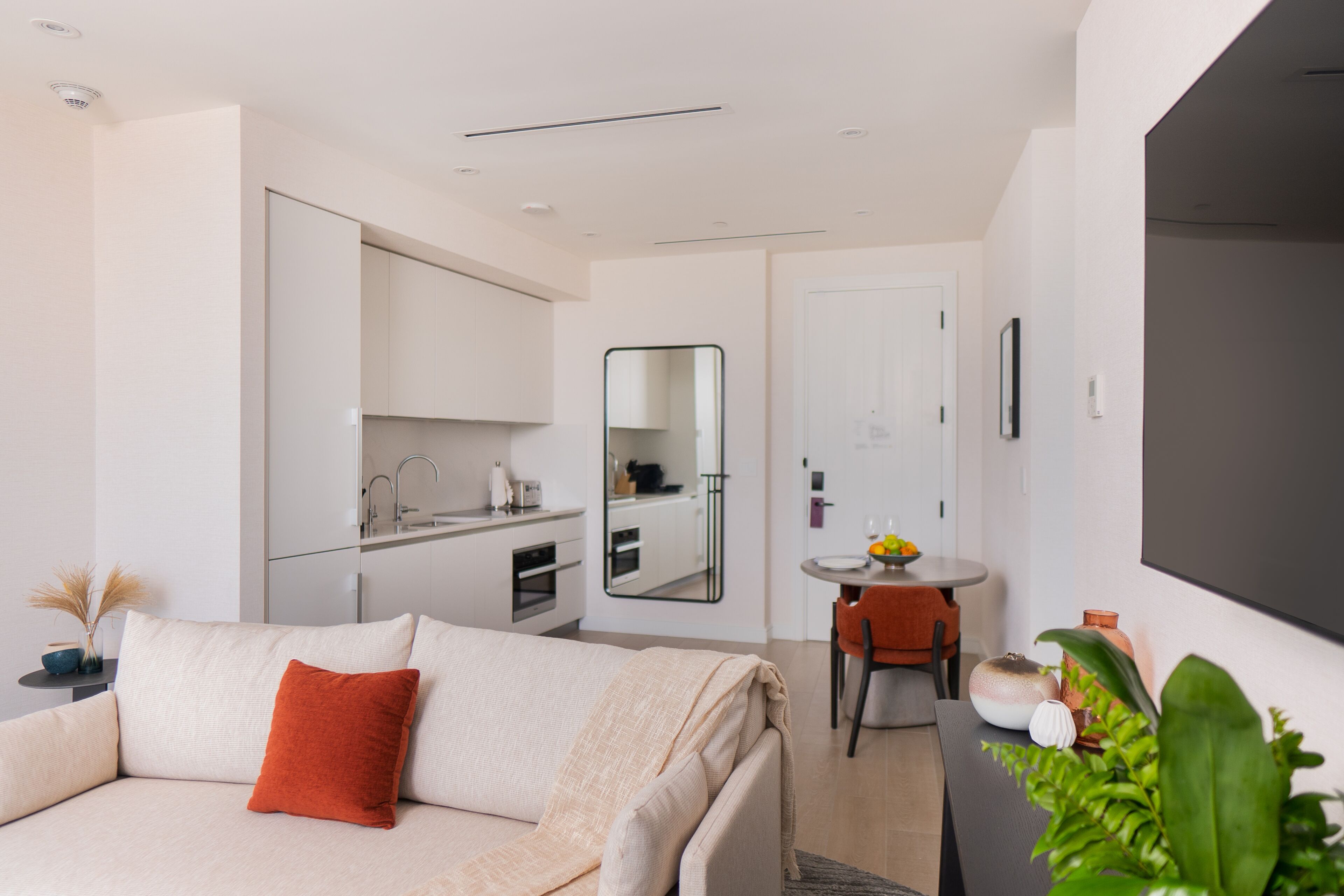 A modern hotel room with a sofa, a dining table, and a kitchen area.