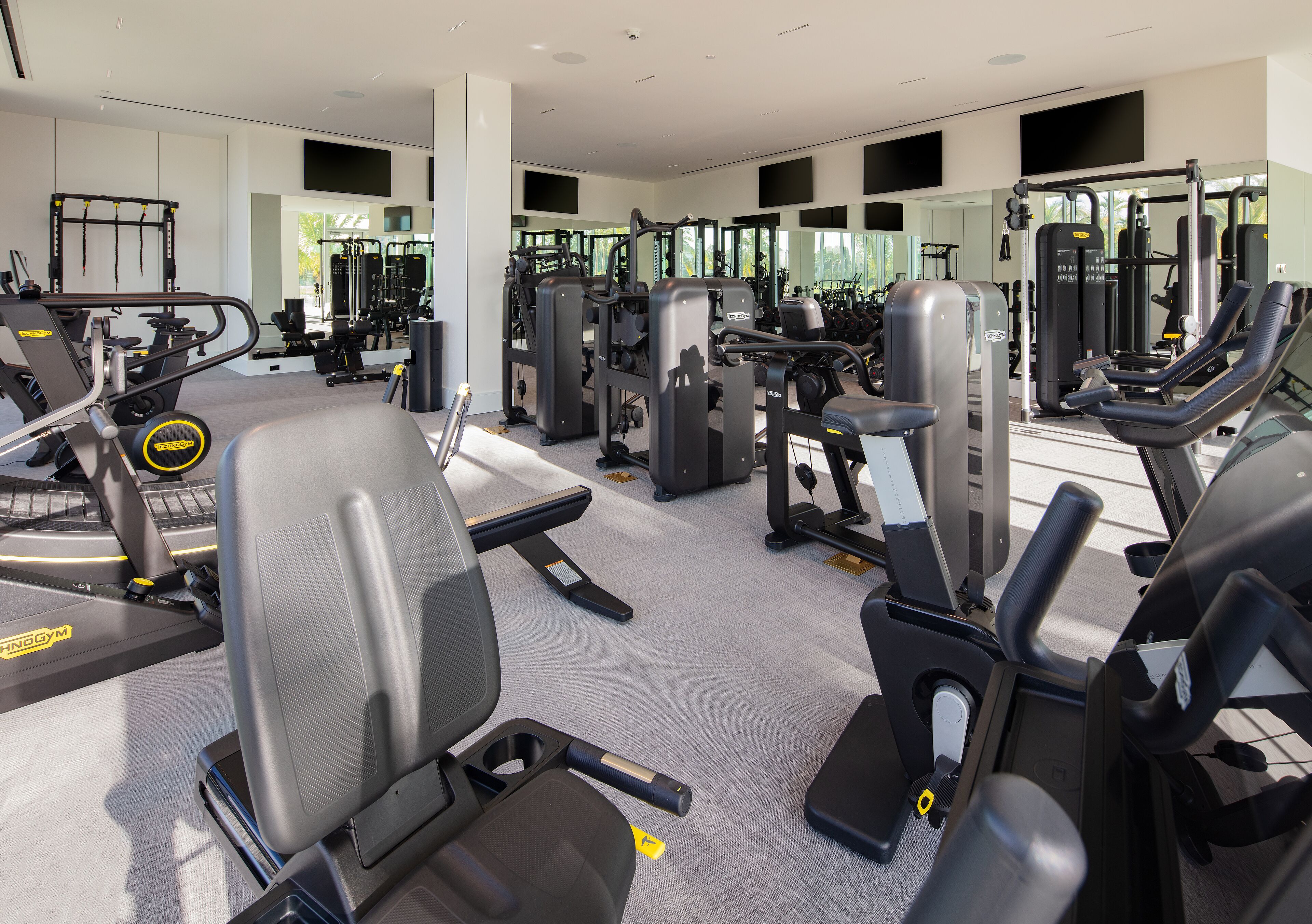 Una palestra moderna con diverse macchine per esercizi, specchi e un'ampia finestra.
