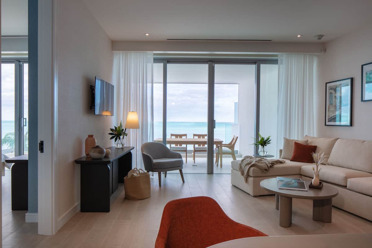 A modern living room with a large window, a sofa, a coffee table, and a TV mounted on the wall.